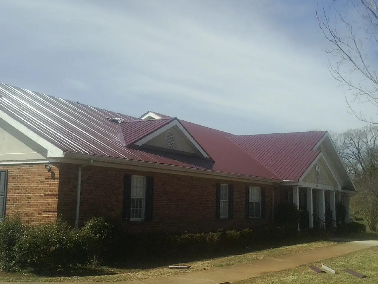Red metal roof with gabled entries on a long brick building, from a Hail Damage Roof Repair job in Mashpee