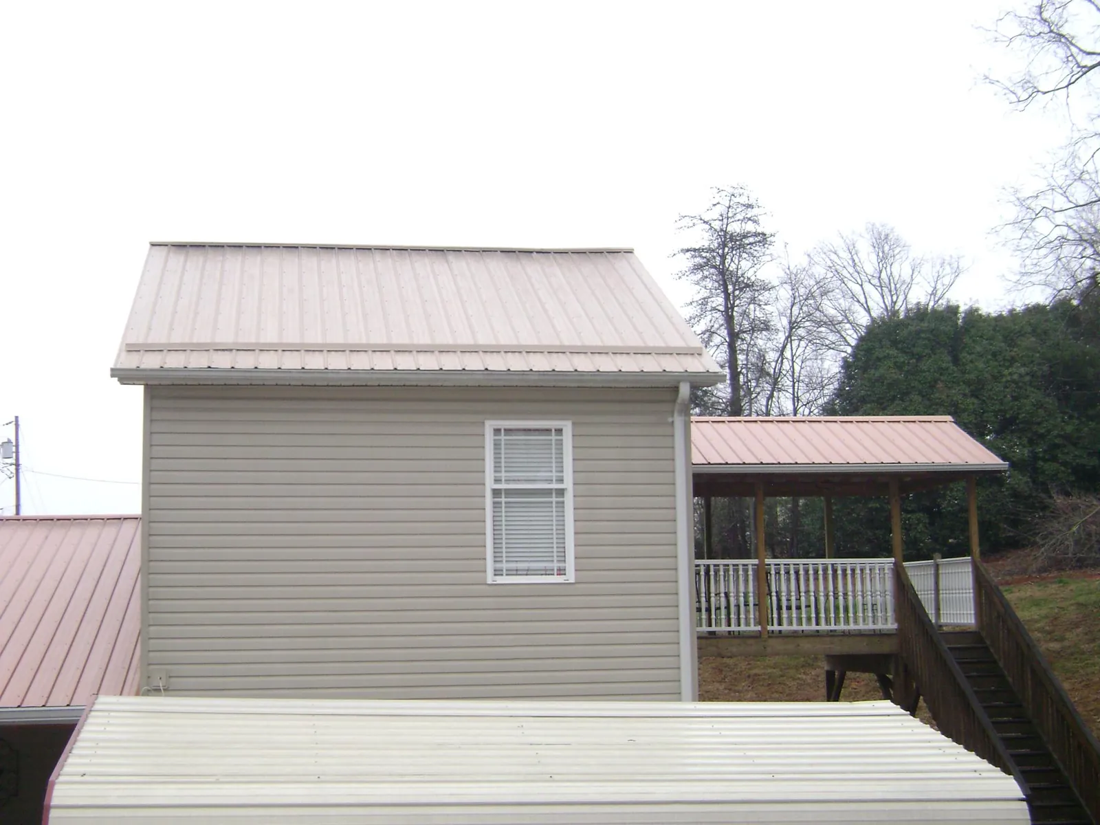 Tan metal roofs on a two story addition and attached porch, from a Roof Replacement job in Mashpee